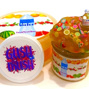 May include: Three containers of colorful slime. One container is filled with orange slime and topped with fruit-shaped decorations and a miniature Evian water bottle. The other two containers have lids with the text "GushMush" and "Fruity Infused Water".
