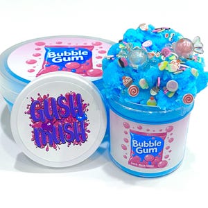 May include: Three containers of blue slime, one open and decorated with candy. The containers have labels that read "Bubble Gum" and "Gush Mush Slime." The slime is a vibrant blue color and is decorated with various colorful candies.