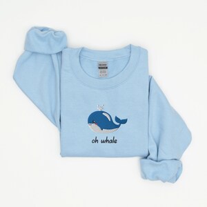 May include: A light blue sweatshirt with an embroidered whale and the text "oh whale" on the front.