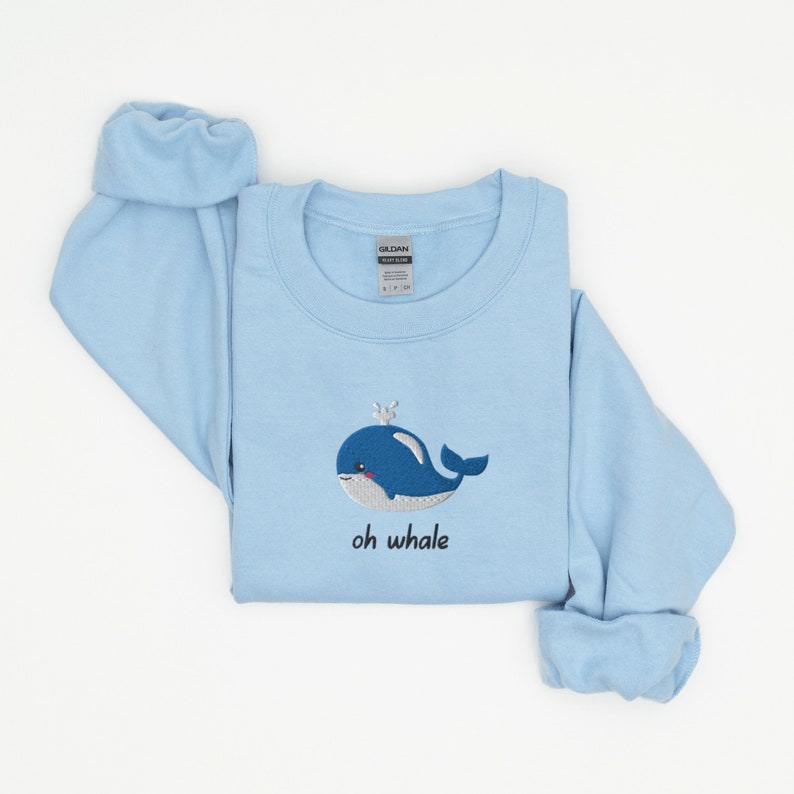 May include: A light blue sweatshirt with an embroidered whale and the text "oh whale" on the front.