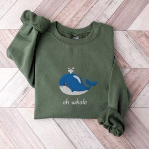 May include: A green sweatshirt with a blue whale embroidered on the front. The whale has a white spout and a white belly. The text "oh whale" is embroidered below the whale.