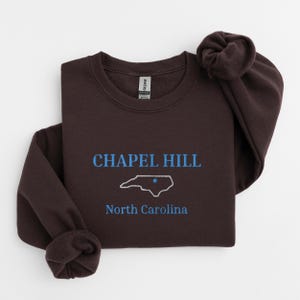Może przedstawiać: Ciemnobrązowa bluza z nadrukiem "Chapel Hill, Karolina P&oacute;łnocna" i konturem stanu Karolina P&oacute;łnocna w kolorze niebieskim.