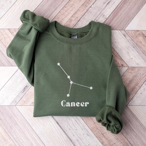 Peut inclure: Un sweat-shirt vert avec une constellation du Cancer brod&eacute;e en blanc et le mot "Cancer" en dessous.