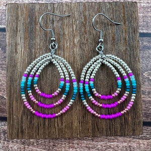 May include: A pair of silver hoop earrings with multiple layers of pink, blue, and teal beads. The earrings have a simple hook closure.
