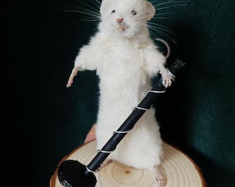 May include: A white taxidermied mouse holding a black and silver mallet. The mouse is standing on a wooden base.
