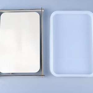 May include: A white rectangular silicone mould for resin casting, next to a wooden frame with a white rectangular piece of paper inside.