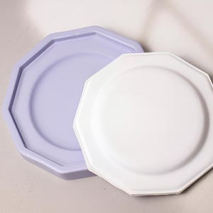 May include: Two octagonal ceramic plates, one white and one light purple, are stacked on top of each other.