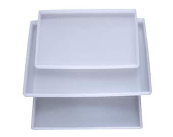 May include: Three white silicone trays of different sizes stacked on top of each other. The trays are rectangular and have a smooth surface.