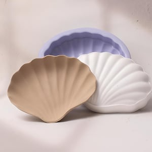 May include: Three seashell-shaped molds, one light blue, one white, and one beige. The molds are made of silicone and are perfect for making soap, candles, or other crafts.