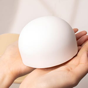 May include: A white ceramic dome shaped object being held in the palm of a hand.