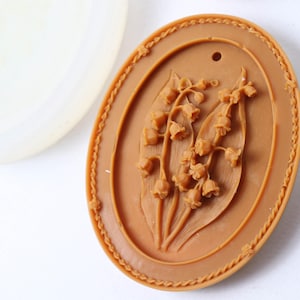 May include: A brown oval-shaped silicone mold with a raised design of lily of the valley flowers.