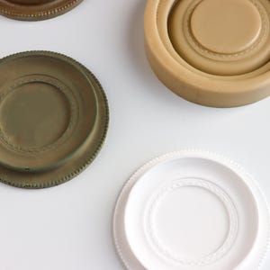 May include: Three round, decorative coasters. One is white with a raised, white rim. One is green with a raised, brown rim. One is brown with a raised, brown rim.