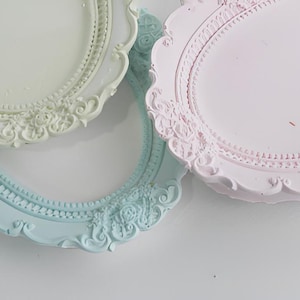 May include: Three ornate, oval decorative trays in pastel shades: white, pale blue, and pink. Each tray has a detailed, raised floral and scrollwork design around the edge, giving a vintage feel.