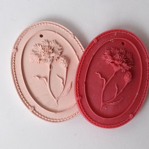 May include: Two oval-shaped decorative plaques with a raised floral design. One plaque is pink with a white flower, and the other is red with a white flower.