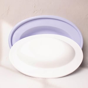 May include: Two oval-shaped ceramic dishes, one white and one light purple, nested together. The white dish is on top of the purple dish.