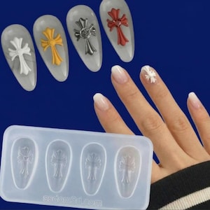Peut inclure: Un moule en silicone rectangulaire avec quatre cavités en forme de goutte, chacune présentant un motif de croix en relief. Le texte ssdom3d.com est gravé sur le moule. Quatre pièces d'art pour ongles finies en blanc, jaune, argent et rouge.
