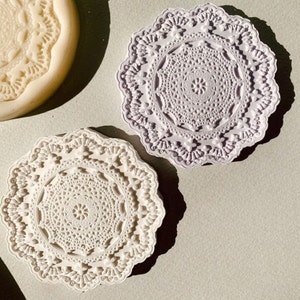 May include: Two white and purple decorative round molds with a lace design. The molds are made of silicone and are perfect for making soap, resin, or other crafts.
