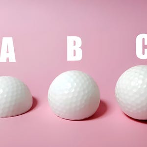 May include: Three white golf balls against a pink background, each labeled with a letter: A, B, and C. The golf balls have a dimpled surface. The background is a solid, light pink color.