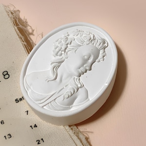 Peut inclure: Sculpture ovale en plâtre blanc d'un buste de femme avec des détails de cheveux et de visage.