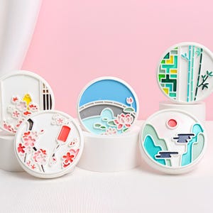 以下が含まれることがあります： 異なるカラフルなデザインの丸い白いコースターが5つ。デザインには、池と蓮の花のある橋、竹林、赤い太陽のある山脈、そして2種類の異なる桜のデザインが含まれています。