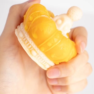 May include: A yellow plastic crown with a white base. The crown has a textured surface and a small white orb on top.