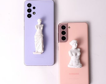 May include: A light purple smartphone and a light pink smartphone, each featuring a white, three-dimensional sculpture of a classical female torso attached to the back. The purple phone has a full-body statue, while the pink phone has a bust.