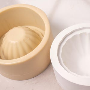 May include: Two silicone molds for baking, one is beige and the other is white. Both molds have a fluted, rounded shape.