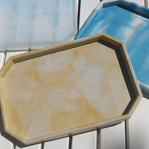 May include: Three decorative trays with a geometric shape. The trays are made of resin and have a marbled design. The trays are in shades of blue, white, and beige.