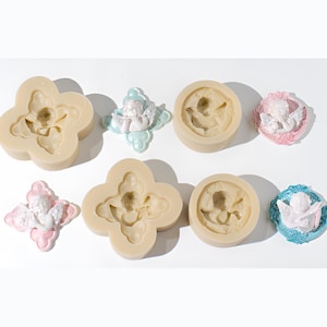 May include: A collection of silicone moulds and finished resin castings featuring cherub figures. The set includes two quatrefoil-shaped moulds, two circular moulds, and four decorative plaques with white cherubs on pink or blue backgrounds.