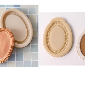 May include: Two silicone molds for making oval-shaped resin crafts. One mold has a simple oval shape, while the other has a decorative beaded border.