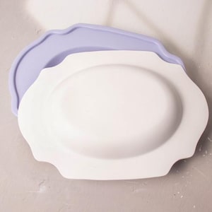 Peut inclure: Un plat de service en céramique blanche avec un bord festonné, niché dans un moule en silicone violet clair.