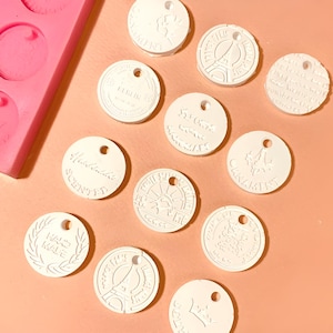 May include: White round ceramic tags with various designs and text, including "Handmade Scents", "Hand Made", "St. Germain", and "Paris". The tags have a hole at the top for hanging.