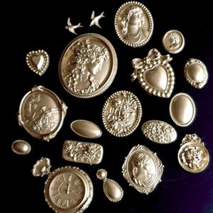 May include: A collection of 18 gold-toned metal embellishments, including hearts, flowers, birds, and portraits. These decorative pieces are perfect for adding a touch of vintage charm to crafts and projects.