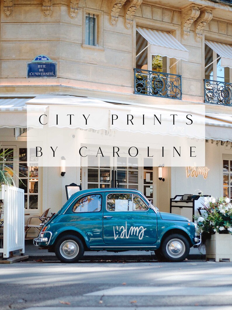 May include: A teal blue Fiat car parked in front of a building with a white awning that says "CITY PRINTS BY CAROLINE". The car has a white sticker on the side that says "Lalma".