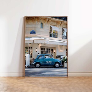 May include: A teal blue vintage car parked in front of a cafe in Paris, France. The car has the word "Calme" written on the side. The cafe has a white awning and a sign that says "Valmy".