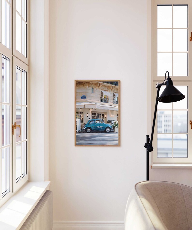 May include: A framed photograph of a blue vintage car parked in front of a building with a white awning. The car has the word "LOVE" written on the side. The building has a sign that says "Le Cafe".