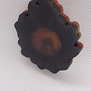 May include: A layered black, red, and gold resin sunflower pendant with a gold chain.