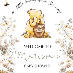 K&ouml;nnte beinhalten: Eine Winnie Puuh Babyparty-Einladung mit einem gelben B&auml;ren, der einen Honigtopf h&auml;lt. Die Einladung hat einen floralen Rand und den Text "a little hunny is on the way!"  "WELCOME TO Marissa's BABY SHOWER JULY. 20TH 2024"