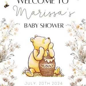 K&ouml;nnte beinhalten: Eine Winnie Puuh Babyparty-Einladung mit wei&szlig;em Hintergrund und floralem Rand. Die Einladung zeigt ein Cartoon-Bild von Winnie Puuh, der einen Honigtopf h&auml;lt. Der Text auf der Einladung lautet "Willkommen zur Babyparty von Marissa" und "Juli 20th 2024".
