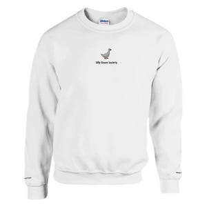 Puede incluir: Sudadera blanca de cuello redondo con un pequeño dibujo de un ganso y el texto "Silly Goose Society". La sudadera es de material suave y tiene puños y dobladillo acanalados. La marca "Gildan" es visible en el cuello.