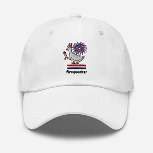 May include: A white baseball cap featuring an embroidered design of a goose wearing a red, white, and blue striped top hat, holding a firework, with a firework burst behind it, a red, white, and blue striped bar, and the text firequacker.