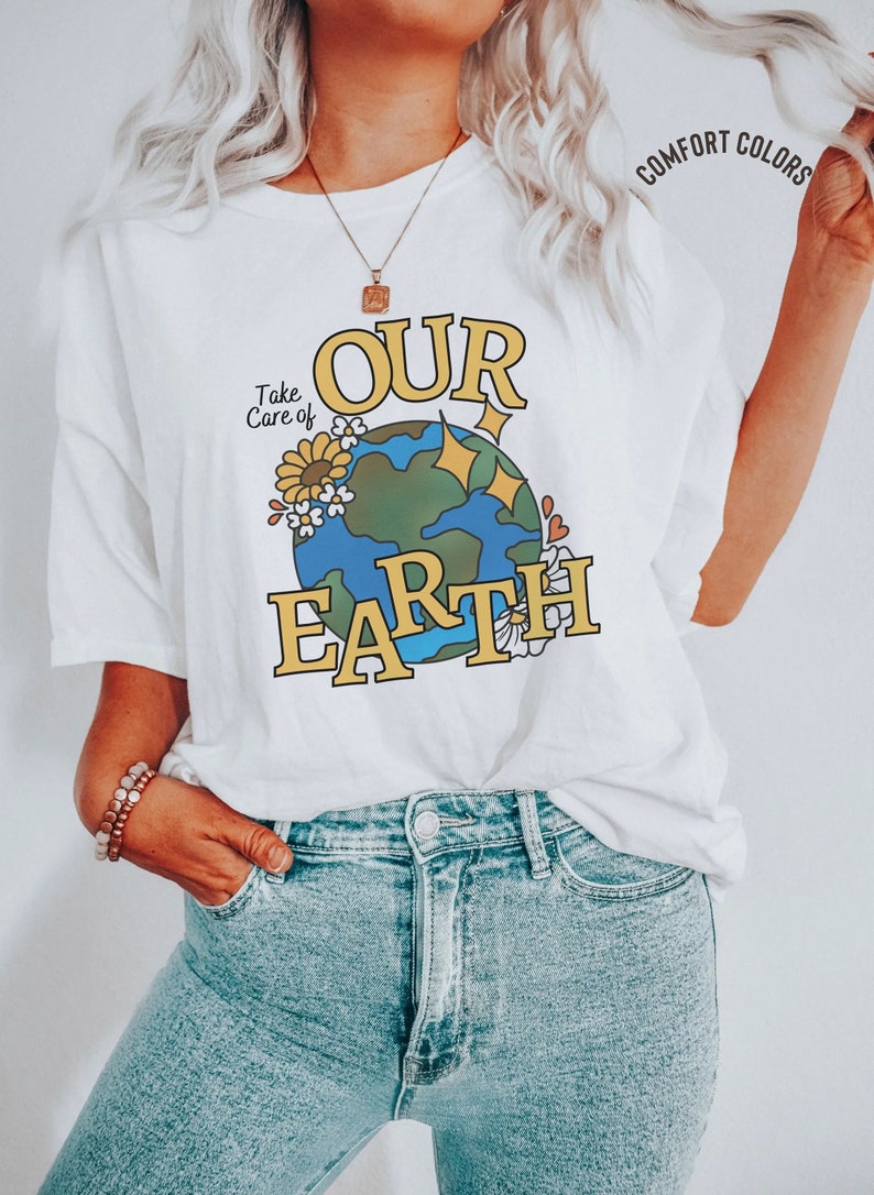 Puede incluir: Camiseta blanca con un gr&aacute;fico de una tierra de dibujos animados con flores y estrellas. El texto "Take Care of Our Earth" est&aacute; impreso en la camiseta.