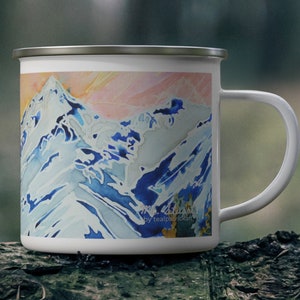 May include: White enamel camping mug with a colorful mountain scene painted on the front. The scene features blue, pink, and white colors. The mug has a silver rim and handle.