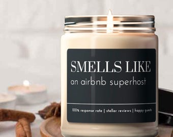 May include: A candle in a glass jar with a black label that reads "SMELLS LIKE an airbnb superhost 100% response rate | stellar reviews | happy guests".