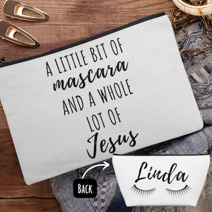 May include: A white canvas makeup bag with a black zipper and the text "A little bit of mascara and a whole lot of Jesus". The back of the bag is white with the text "Linda" and two black eyelashes.