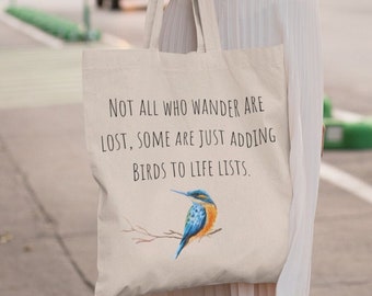 May include: A white canvas tote bag with a blue and green bird illustration and the text "NOT ALL WHO WANDER ARE LOST, SOME ARE JUST ADDING BIRDS TO LIFE LISTS."