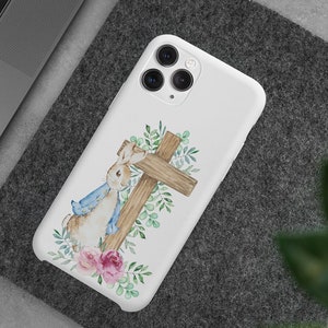 May include: White phone case with a watercolor illustration of a rabbit leaning against a wooden cross with green leaves and pink flowers.