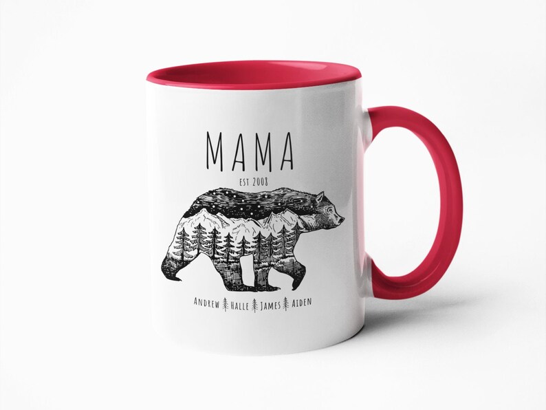 May include: White ceramic mug with a red rim and handle. The mug has a black and white illustration of a bear with a mountain range and trees inside its silhouette. The text "MAMA EST 2000" is above the bear and the text "ANDREW HALLE JAMES AIDEN" is below the bear.