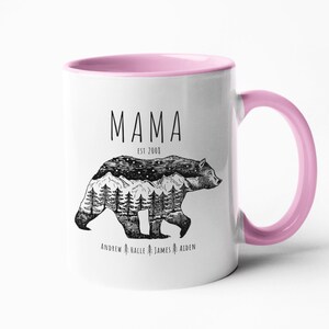 May include: White ceramic mug with a pink rim and handle. The mug features a black and white illustration of a bear with a mountain range and stars inside. The text "Mama Est 2003" is above the bear and the text "Andrew Halle James Aiden" is below the bear.