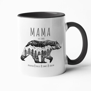 May include: White ceramic mug with a black rim and handle. The mug features a black and white illustration of a bear with mountains and trees inside its silhouette. The text "MAMA EST 2008" is printed above the bear and the names "ANDREW HALLE JAMES AIDEN" are printed below the bear.
